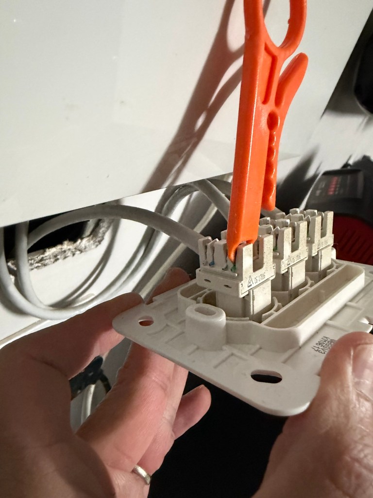 Using an Ethernet punch-down tool to re-seat network cable wires in a wall socket during a DIY home internet repair.